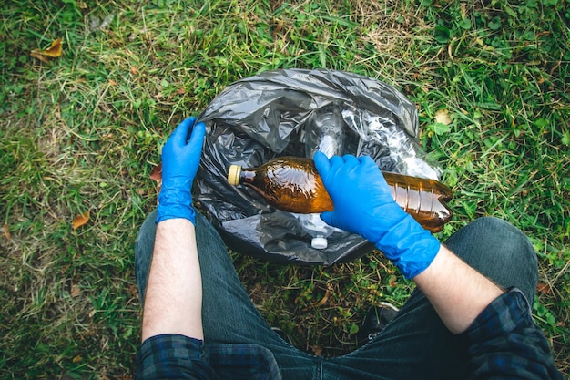 Free photo a man cleans up the forest throws a bottle into a trash bag closeup