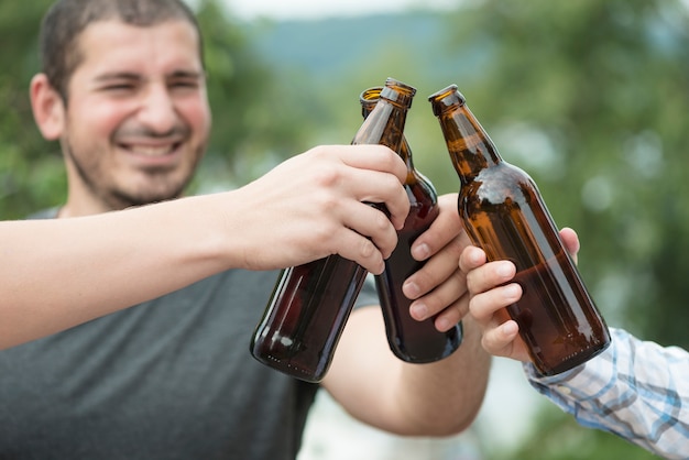 Man clinking bottle with friends in nature