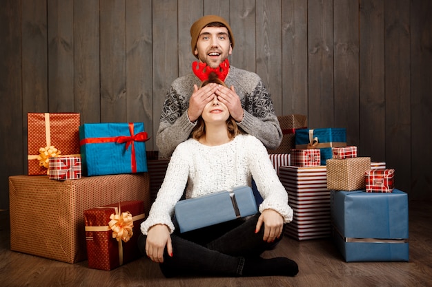 Free photo man close his girlfriend's eyes with hands over wooden wall