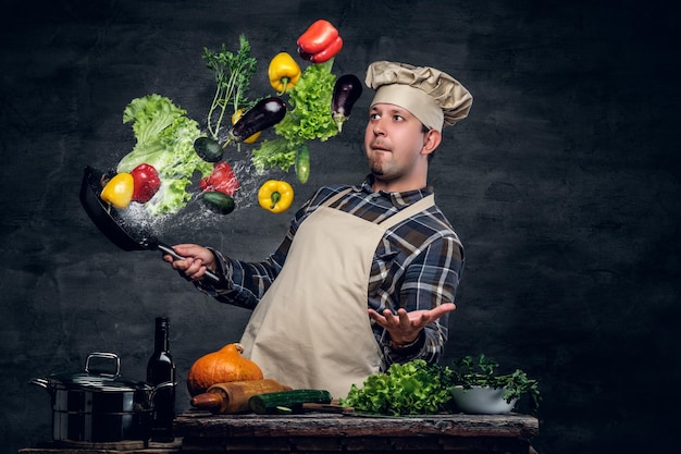 Free photo man cook holds a pan with vegetables flying in the  air.