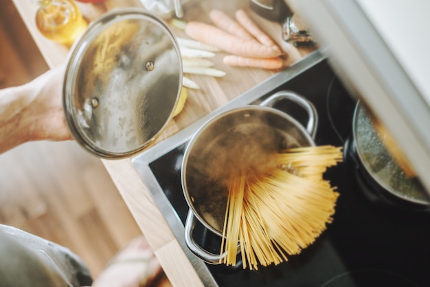 Free photo man cooking pasta spaghetti at home in the kitchen. home cooking or italian cooking concept.