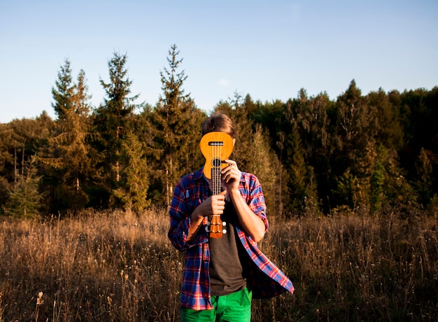 Free Photo man covering his face with ukulele guitar