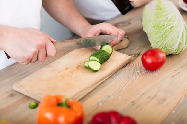 Free photo man cutting the cucumber on a wooden plate