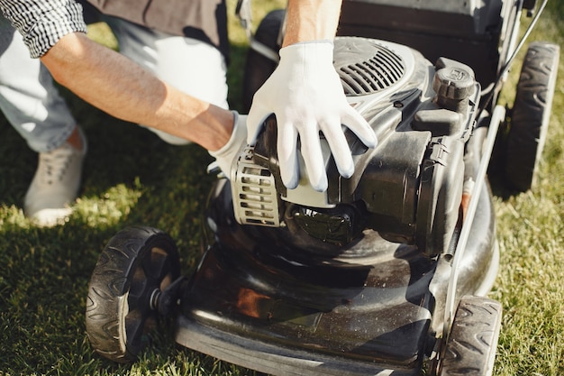 Free photo man cutting grass with lawn mover in the back yard. male in a black apron. guy repairs.