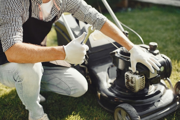 Free photo man cutting grass with lawn mover in the back yard. male in a black apron. guy repairs.