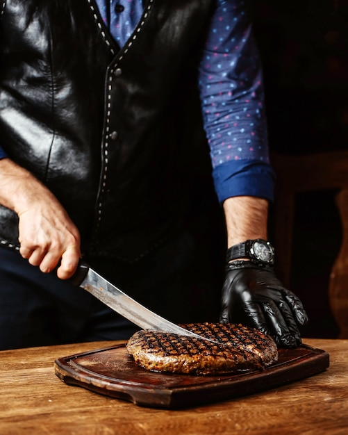 Free photo man cutting steak in round shape wearing black gloves