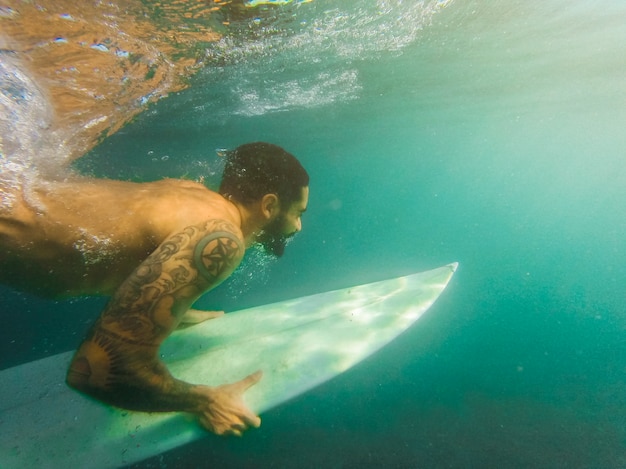 Man diving with white surfboard underwater