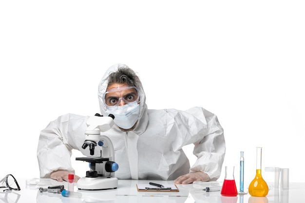 man doctor in protective suit and with mask using microscope on white