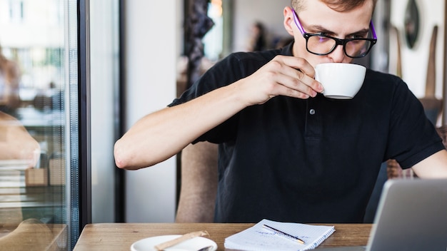 Free Photo man drinking coffee at table with laptop 