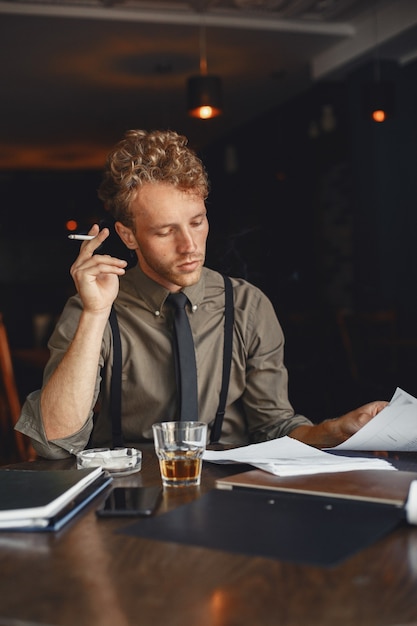 Man drinks whiskey. Businessman reads documents. Director in a shirt and suspenders.