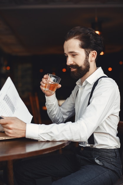 Free photo man drinks whiskey. businessman reads documents. director in a shirt and suspenders.