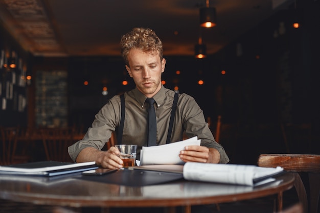 Free photo man drinks whiskey. businessman reads documents. director in a shirt and suspenders.