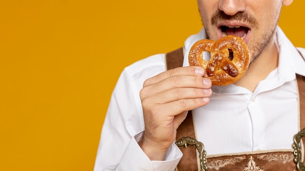 Free Photo man eating german pretzel with yellow background