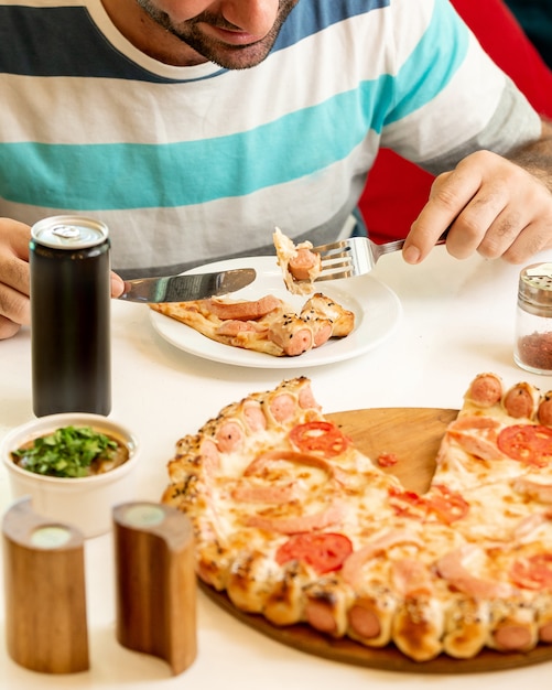 Free photo man eating a slice of sausage pizza  at the restaurant