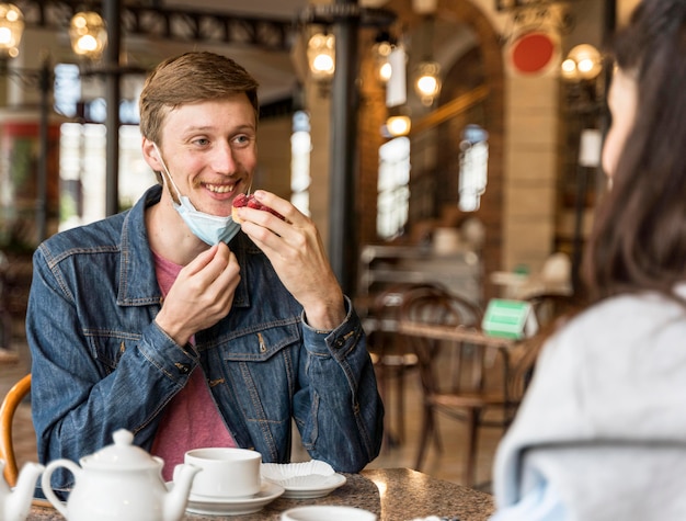 Man eating some cake at the restaurant while wearing his face mask on his chin