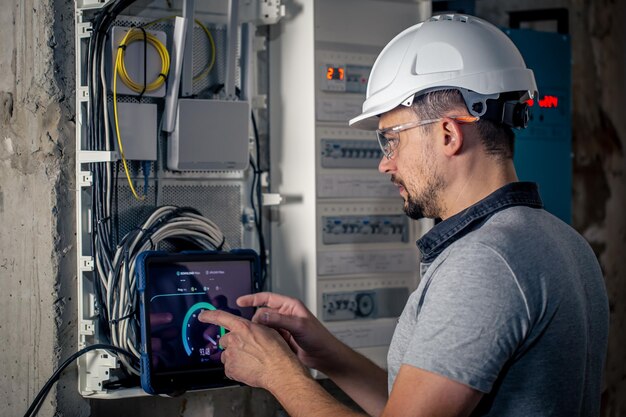 Man an electrical technician working in a switchboard with fuses uses a tablet