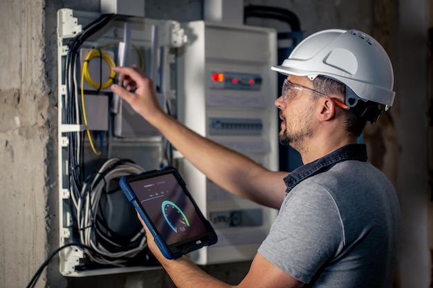 Free photo man an electrical technician working in a switchboard with fuses uses a tablet