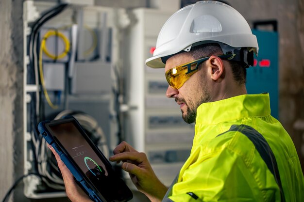 Man an electrical technician working in a switchboard with fuses uses a tablet