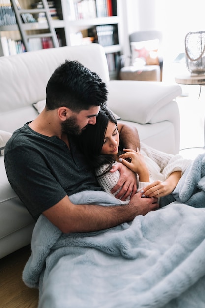 Man embracing her girlfriend holding hand sitting near sofa