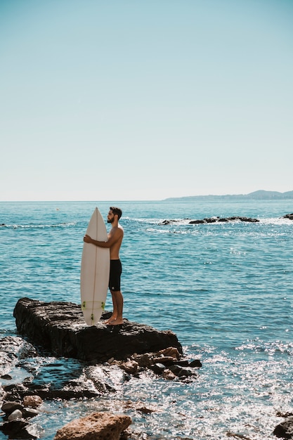 Man embracing surfboard on stone