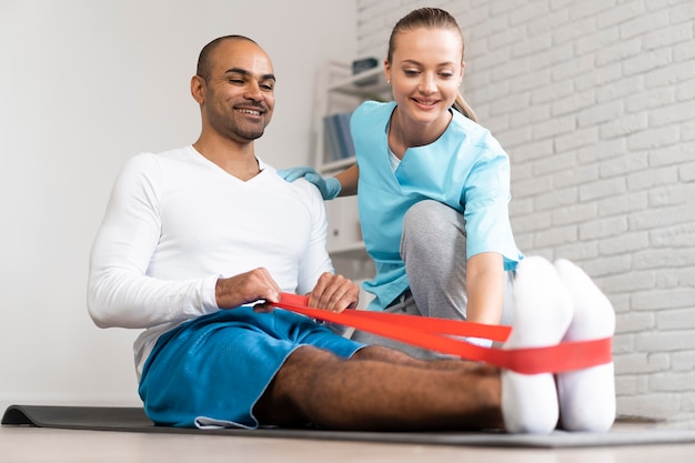 Man and female physiotherapist doing exercises with elastic band