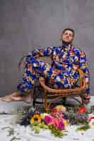 Free photo a man in floral dress sitting on chair with different flowers on floor