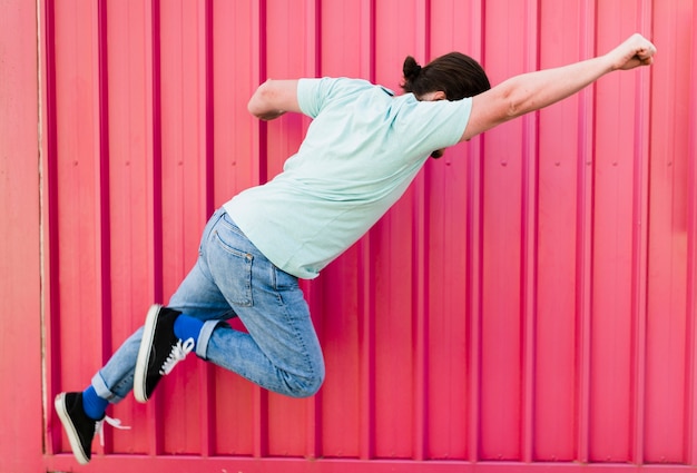 Man flying with arms raised against pink corrugated wall