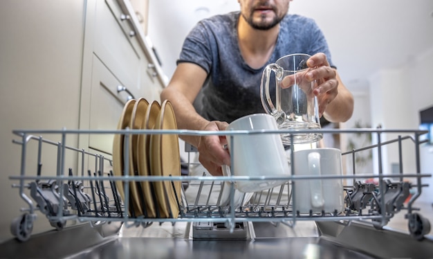 Free photo a man in front of an open dishwasher takes out or puts down dishes.