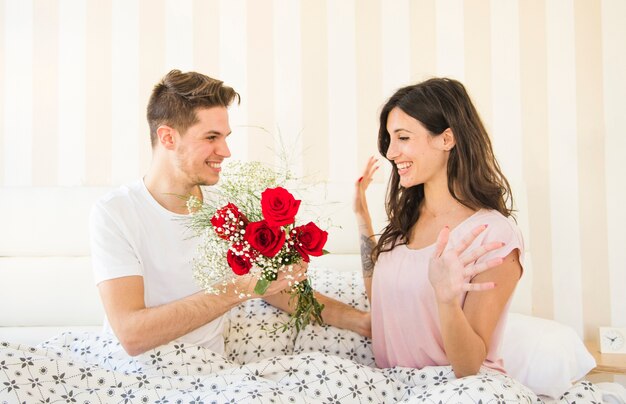 Man giving flowers to woman on bed