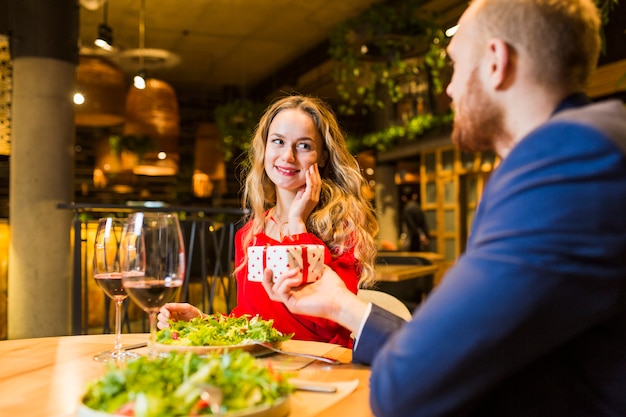 Man giving small gift box to blond woman at table