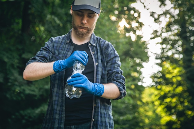 Free Photo a man in gloves with a plastic bottle in his hands cleans the forest