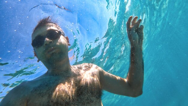 Man in goggles swimming under the blue and transparent water of the Mediterranean sea. Holding the camera