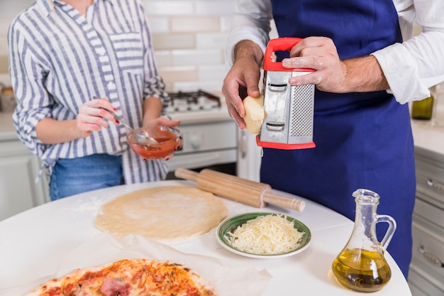 Free photo man grating cheese for pizza with woman in kitchen