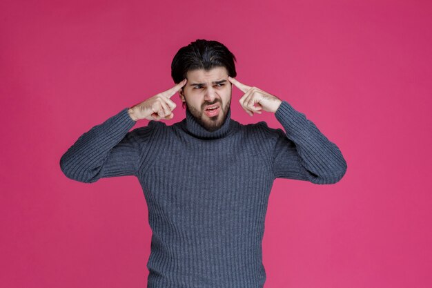 Man in grey sweater putting his fingers to the head as he is thinking.