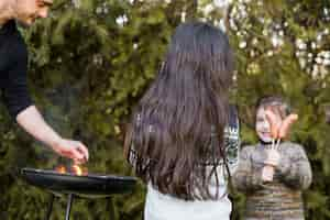 Free photo man grilling outdoors with two daughters