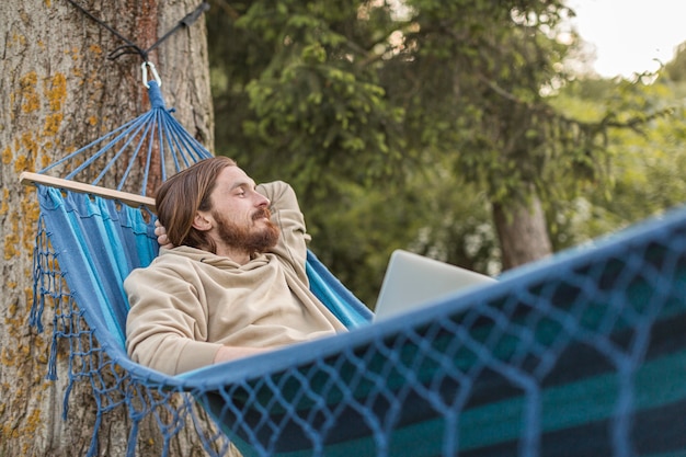 Free photo man in hammock enjoying nature with laptop