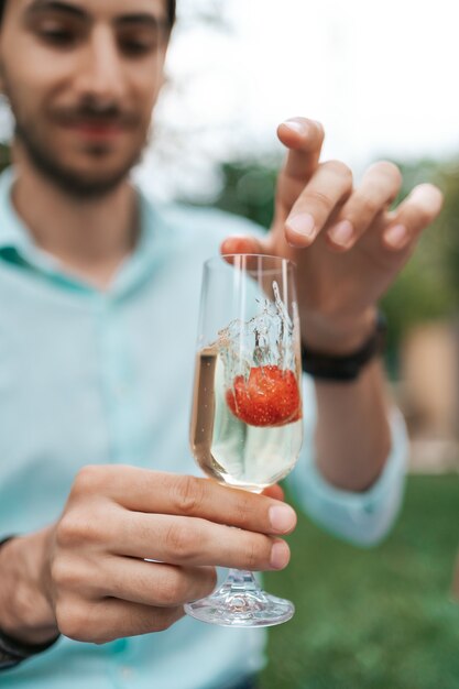 Man hand drop a strawberry in a glass with sparkling wine. Beautiful life, cellebration