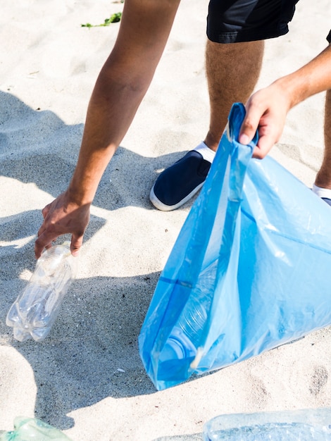 Free Photo man hand picking plastic bottle while holding blue garbage bag on beach