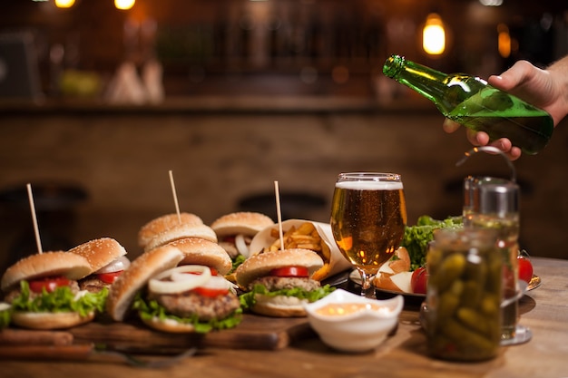 Free Photo man hand pours larger beer in a glass standing on a vintage table .blurred counter bar . jar of pickles.