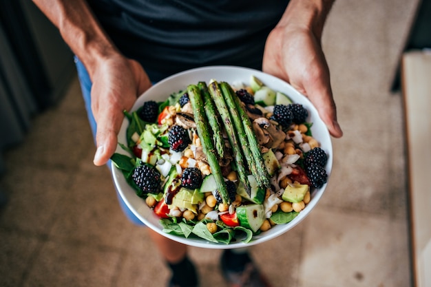 Free photo man hands holding big deep plate full of healthy paleo vegetarian salad made from fresh organic biological ingredients, vegetables and fruits, berries and other nutritional things