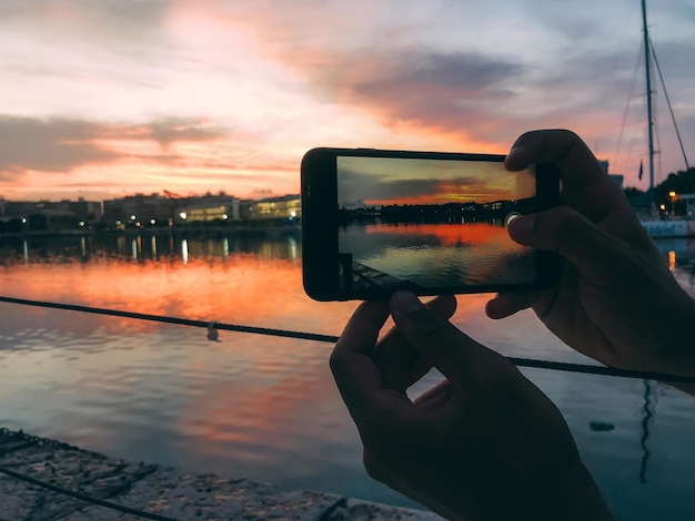 Free Photo man hands taking a picture with mobile phone of a sunset