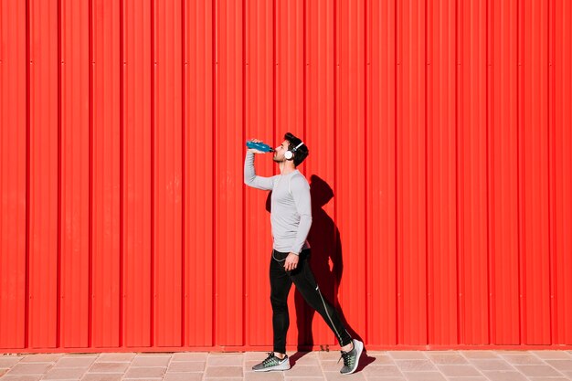 Man in headphones drinking water near wall