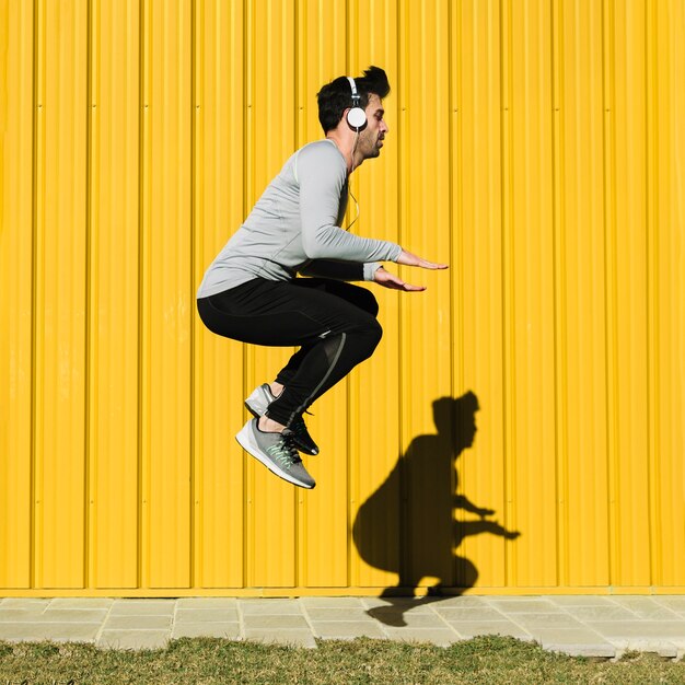 Man in headphones jumping near yellow wall