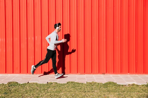 Man in headphones running near red wall