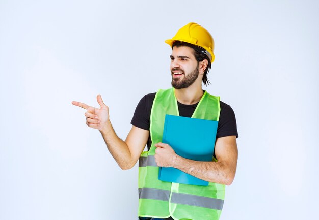 Man in helmet holding a blue folder and pointing someone on the left.