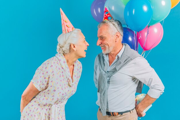 Man hiding birthday gift from his wife on blue backdrop