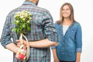 Free photo man hiding a gift box and flower behind his back giving surprise to girlfriend