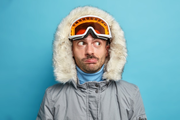 Free Photo man hiker looks thoughtfully aside wears ski goggles and winter jacket with hood has active rest during vacation enjoys favorite sport.