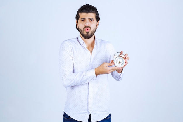 Free photo man holding an alarm clock and confused as he is late