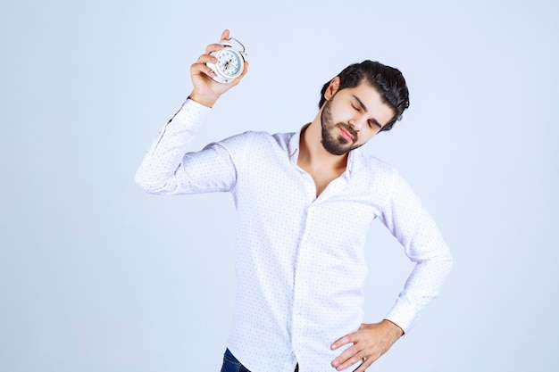 Free photo man holding an alarm clock and looks still sleepy